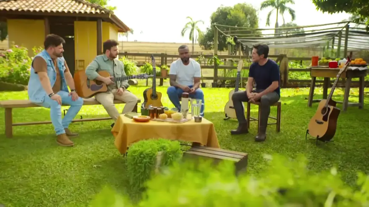 Luiz Cláudio & Giuliano e Alexandre Pires sentados ao lado de Daniel, na área externa de uma Fazenda, rodeados por uma mesa com café da manhã em uma área verde